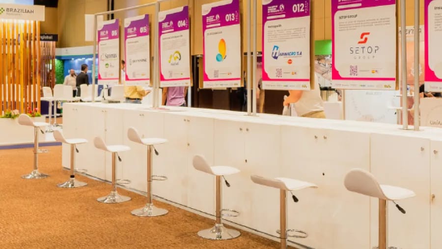 Row of business stands with white counters, stools and numbered company posters